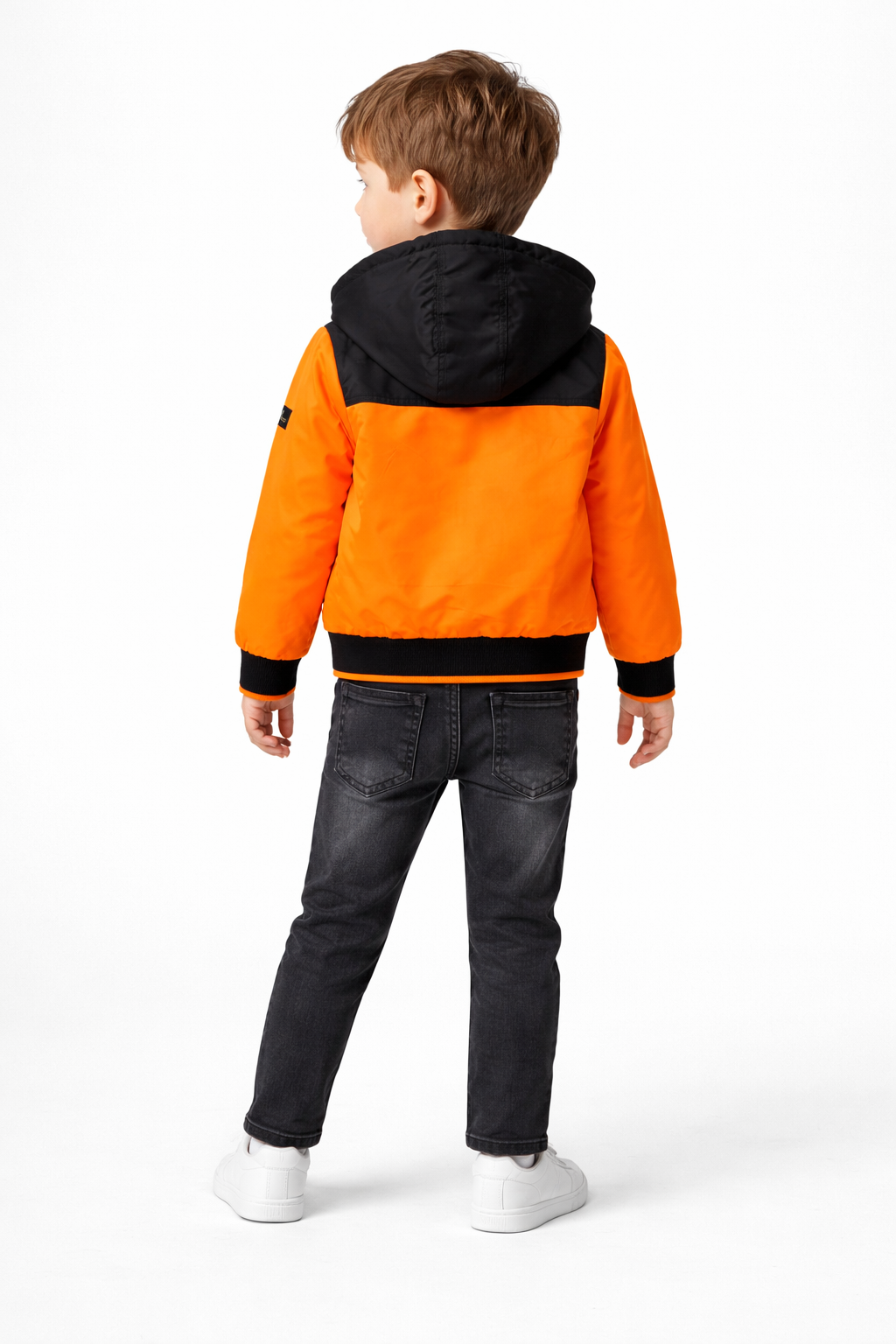 A back view of a young boy modeling the stylish orange and black hooded jacket and dark denim jeans from the NYC-themed 3-piece set at Trendy Angels Boutique.