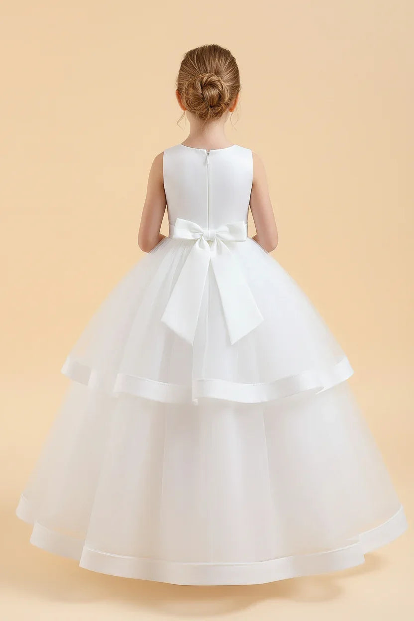Rear view of an elegant white flower girl gown showing a clean satin bodice with a large structured back bow and a voluminous tiered tulle skirt.