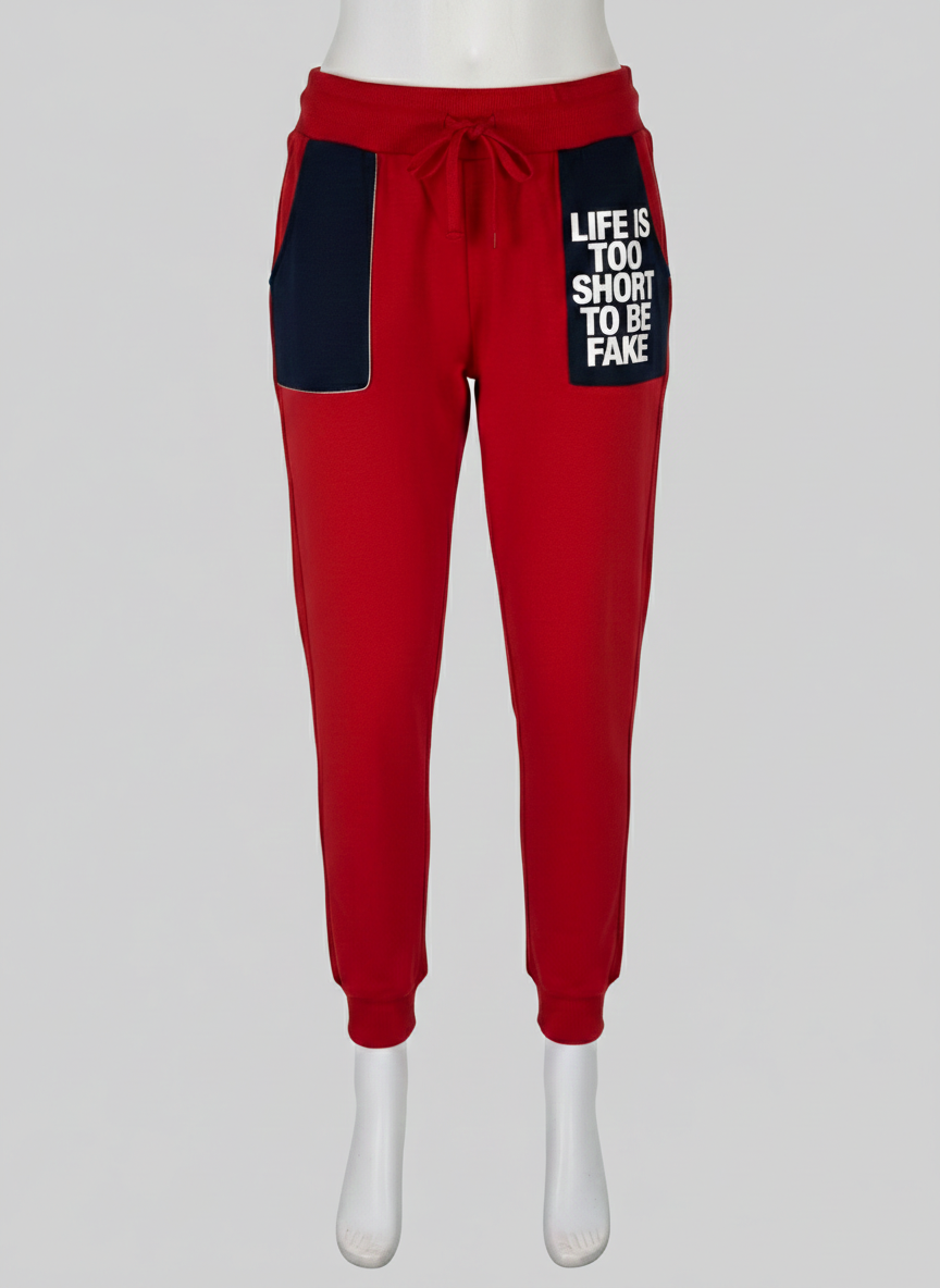 Full view of tapered vibrant red joggers featuring a deep dark navy contrast pocket with white bold text reading "Life is too short to be fake" at Trendy Angels Boutique in Brunswick.
