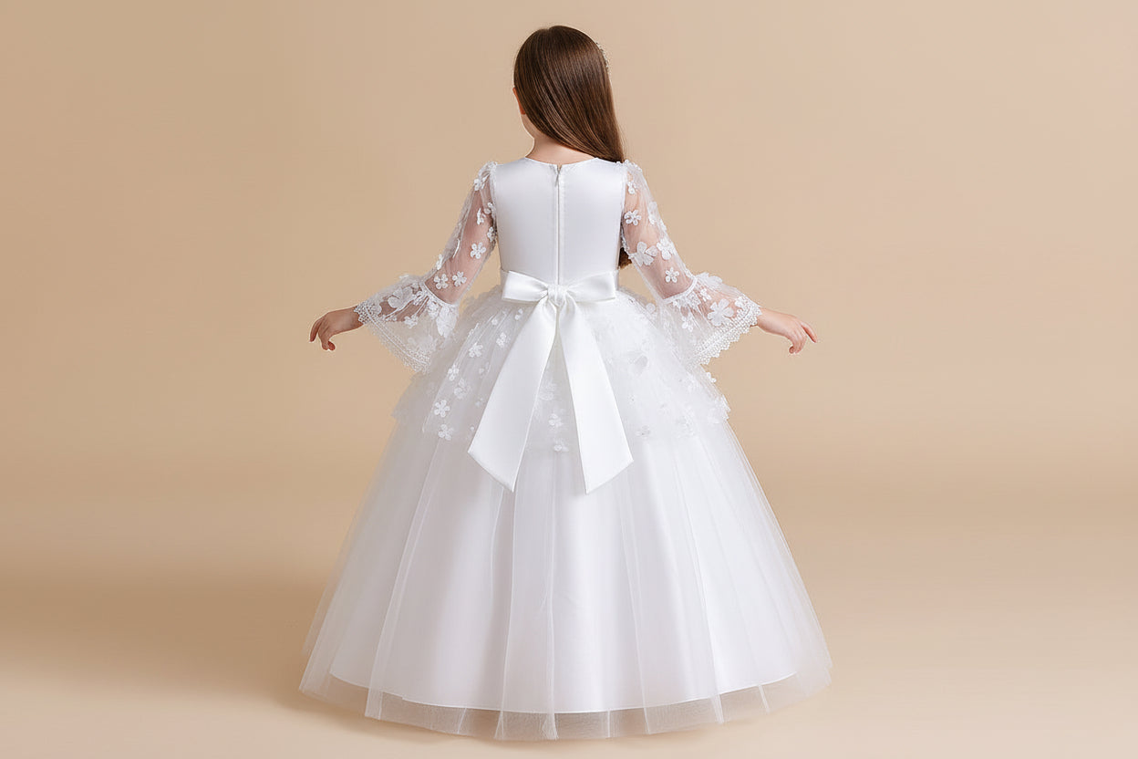 Front view of a young girl wearing a white floor-length communion dress featuring a lace bodice, long floral wing sleeves, and a tiered tulle skirt at Trendy Angels Boutique.