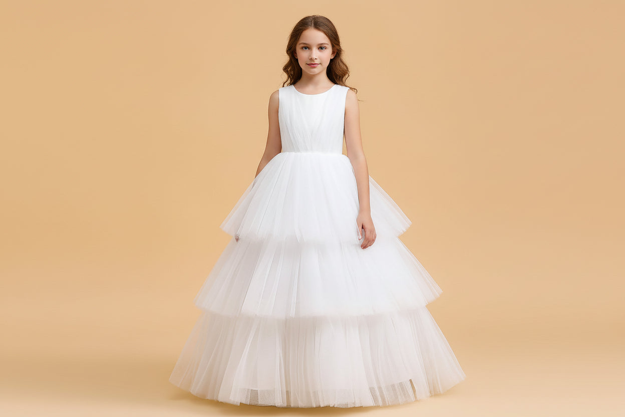 Elegant white flower girl dress featuring a pleated sleeveless bodice and a voluminous three-tier tulle skirt, available at Trendy Angels Boutique.