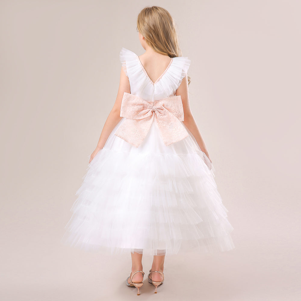 Rear view of an elegant white tiered tulle flower girl dress featuring a deep V-back and a statement pink lace bow. Shop this look at Trendy Angels Boutique, 533 Sydney Rd Brunswick Melbourne. For details, call 04 19 19 19 09.