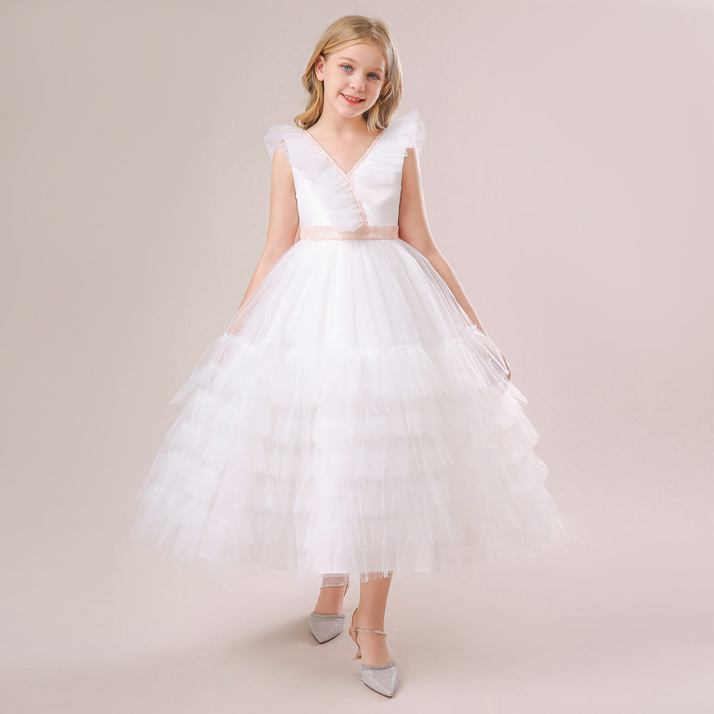 A young girl modeling a white sleeveless flower girl dress featuring a V-neckline, tiered ruffle tulle skirt, and a delicate pink satin waist belt. Available at Trendy Angels Boutique located at 533 Sydney Rd, Brunswick Melbourne. For inquiries, call 04 19 19 19 09.