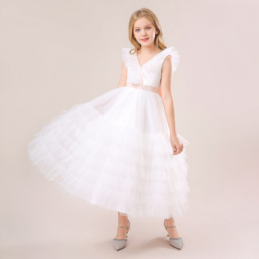 A young girl modeling a floor-length white tulle flower girl dress featuring a pleated bodice and a delicate white satin bow at the waist. Available at Trendy Angels Boutique, 533 Sydney Rd Brunswick Melbourne. For inquiries, call 04 19 19 19 09.