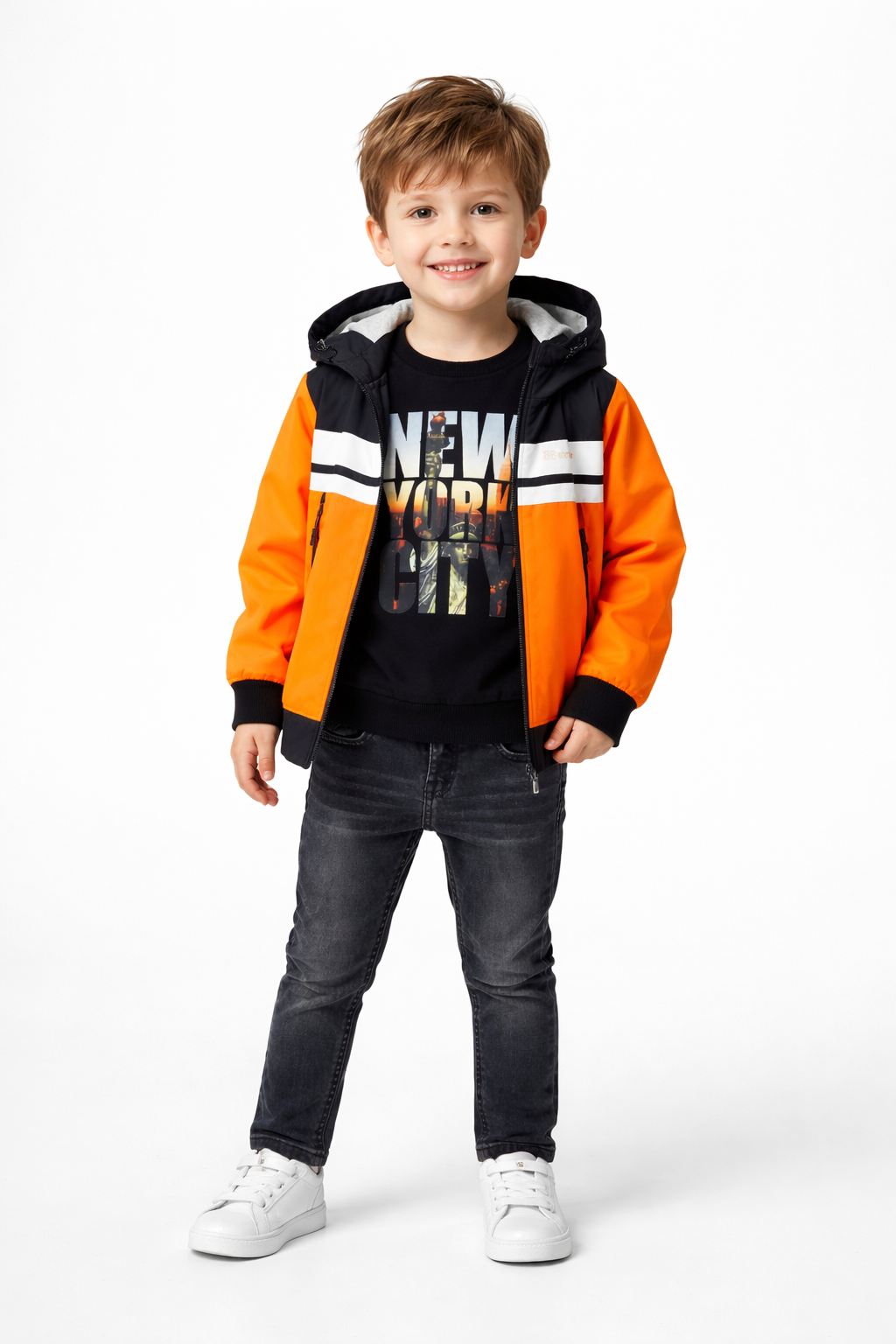 A young boy modeling a stylish NYC-themed winter outfit, featuring a vibrant orange and black hooded jacket paired with coordinated casual wear from Trendy Angels Boutique.