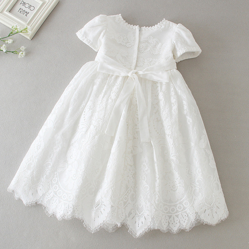Back view of a white floral lace baby girl baptism dress with a large silk ribbon bow and scalloped hemline, available at Trendy Angels Boutique in Brunswick.