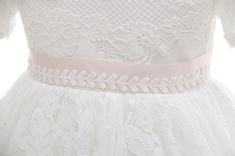 High-detail view of a soft pink waist ribbon on a floral lace christening gown, featuring intricate vine embroidery for a traditional baby girl baptism look.