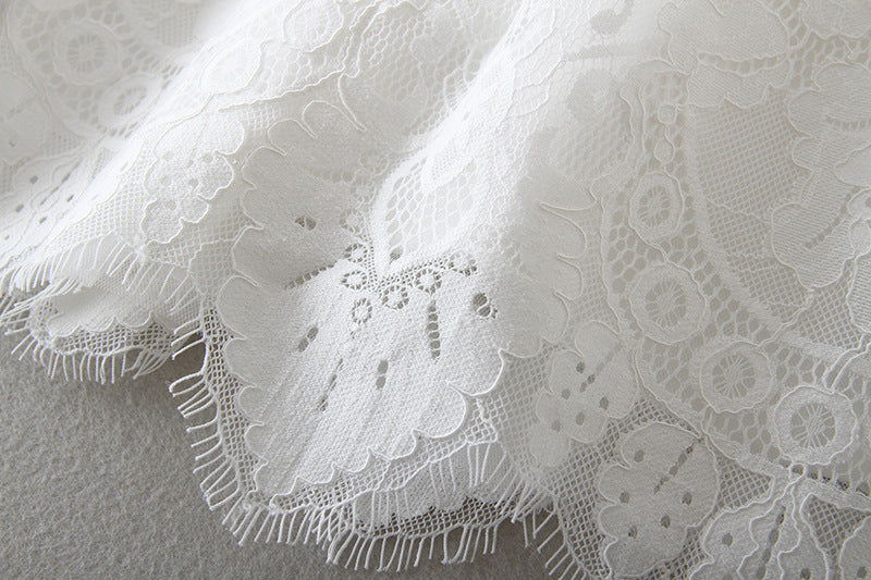 A high-detail close-up of the intricate white floral lace and scalloped eyelash hemline on a baby girl's baptism dress, available at Trendy Angels Boutique, 533 Sydney Rd Brunswick Melbourne.