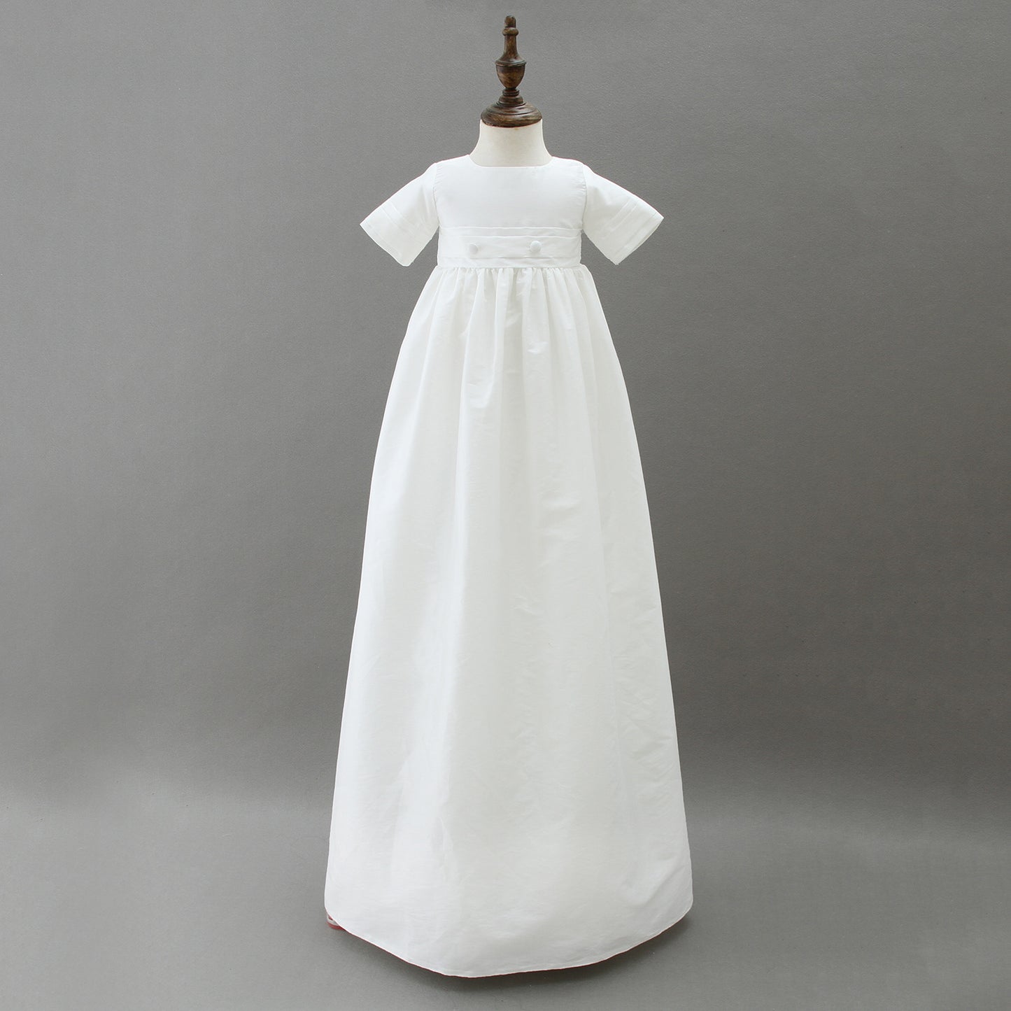 A full-length traditional white boys' baptism gown with a matching pleated hat displayed on a mannequin, showcasing the timeless design available in Melbourne.