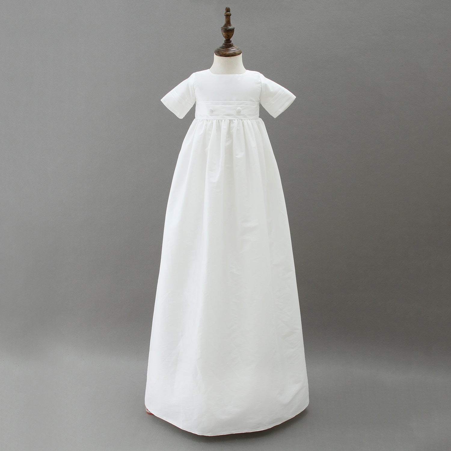 A full-length traditional white boys' baptism gown with a matching pleated hat displayed on a mannequin, showcasing the timeless design available in Melbourne.