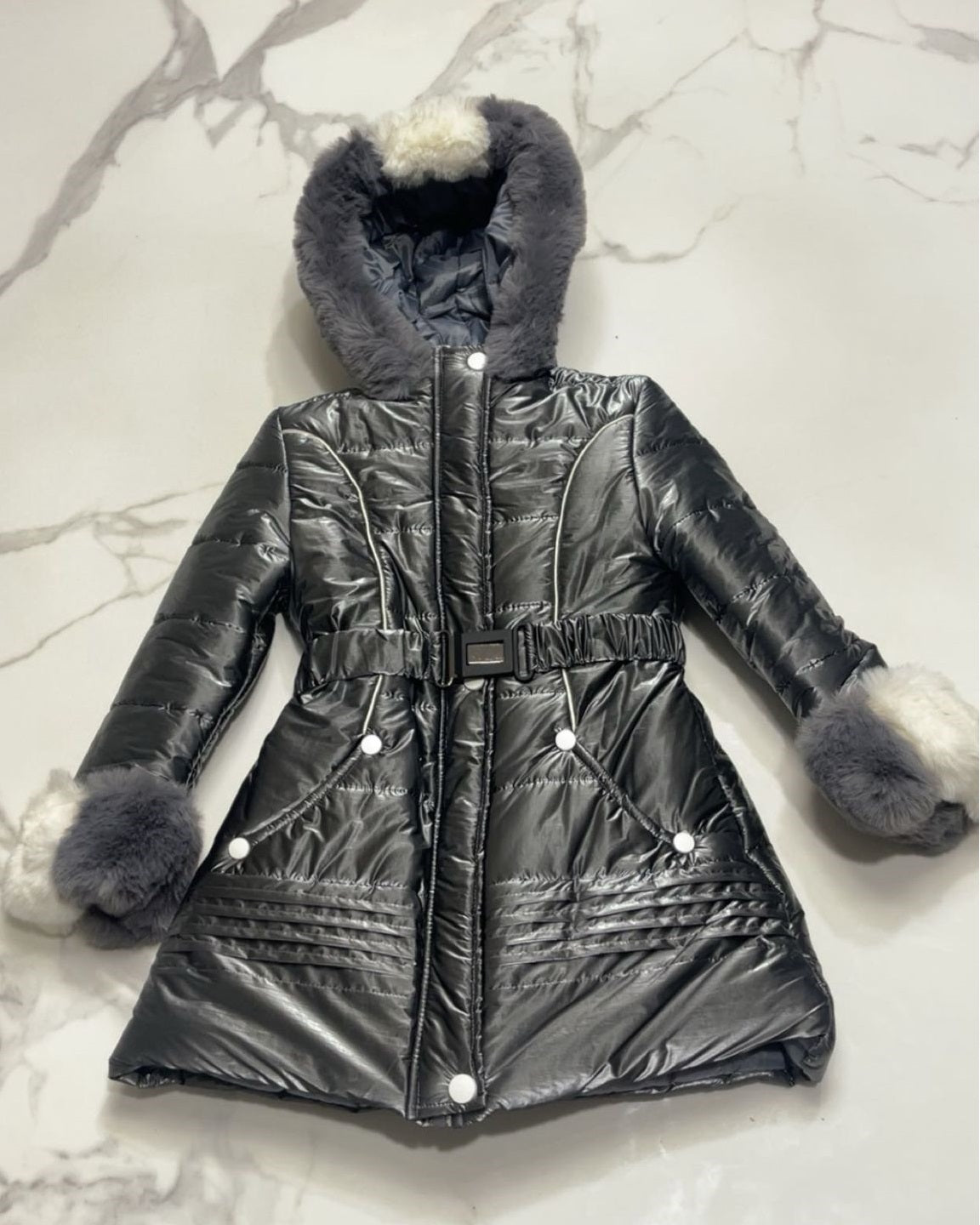 Flat lay view of girls black puffer jacket with dual-tone grey and white faux fur trim and adjustable buckle belt.