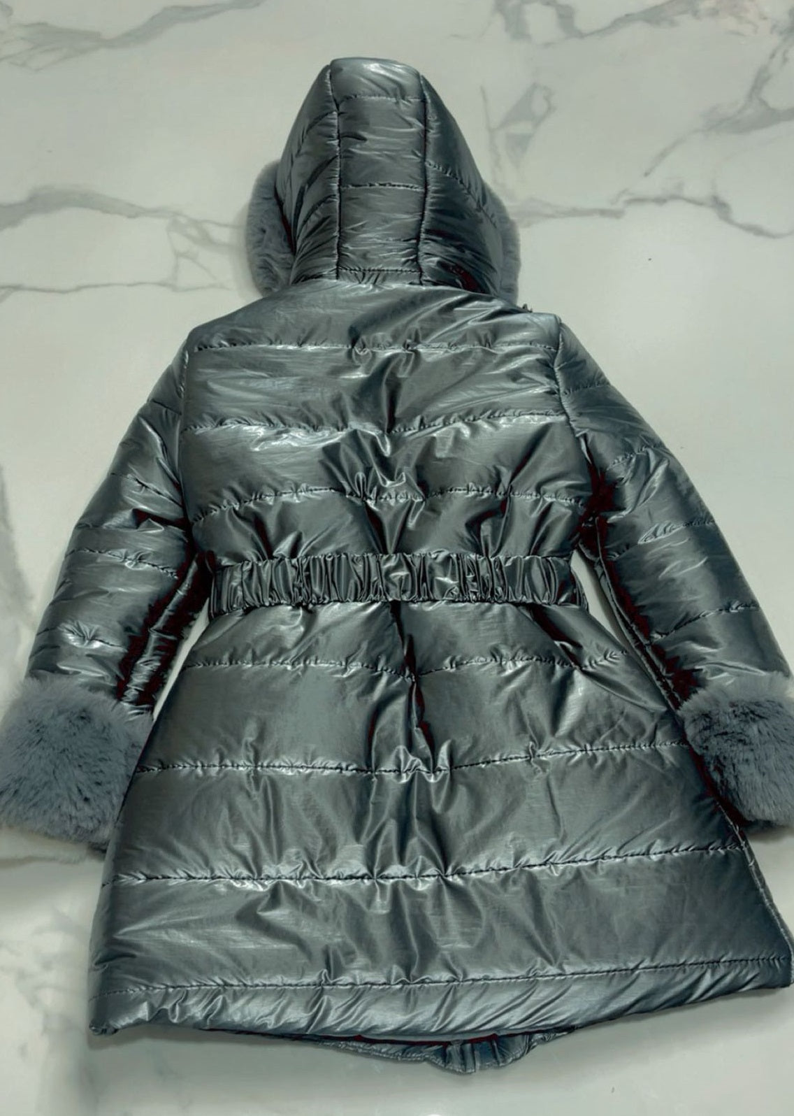 Rear view flat lay of girls black quilted puffer jacket with elasticated waist and plush faux fur hood detail.