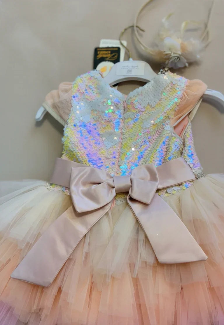Back view of a luxury rainbow celebration dress showcasing a large, champagne-colored satin bow and a multi-layered, voluminous tulle skirt in ombré pastels. Highlights the elegant drape of the long floral wing sleeves. Hand-crafted for special occasions. Visit our boutique at 533 Sydney Rd, Brunswick, Melbourne or contact us at 04 19 19 19 09
