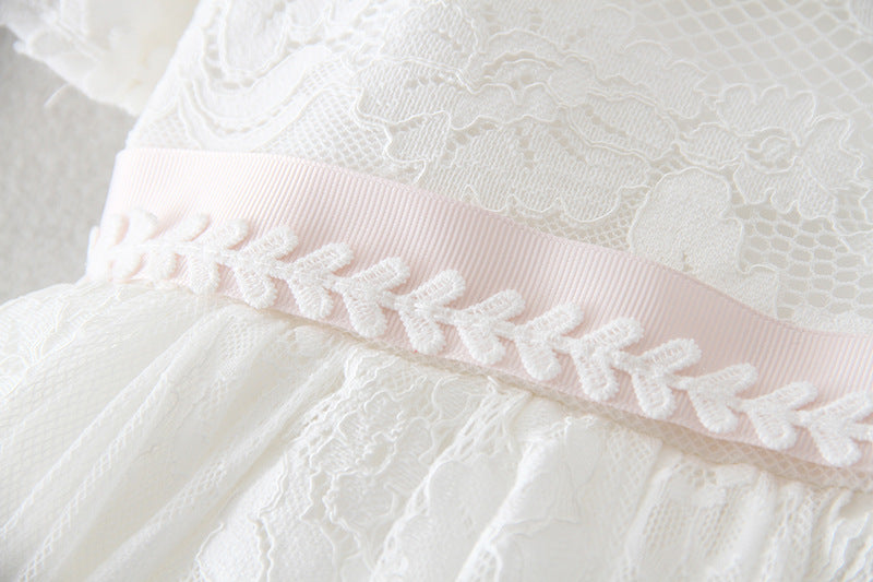 Close-up of a delicate pink satin ribbon sash with embroidered leaf detailing on a white lace baptism dress, available at Trendy Angels Boutique in Brunswick.