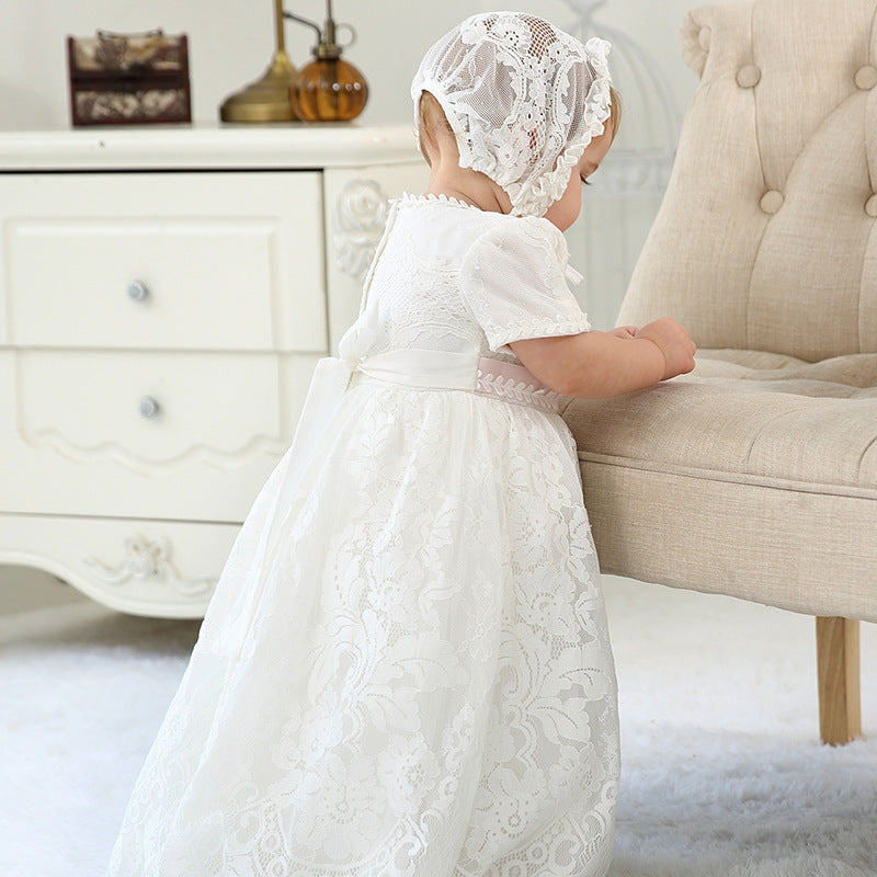 A white floral lace baby girl baptism dress with a pink ribbon sash displayed on a mannequin, showcasing the intricate lace detail.