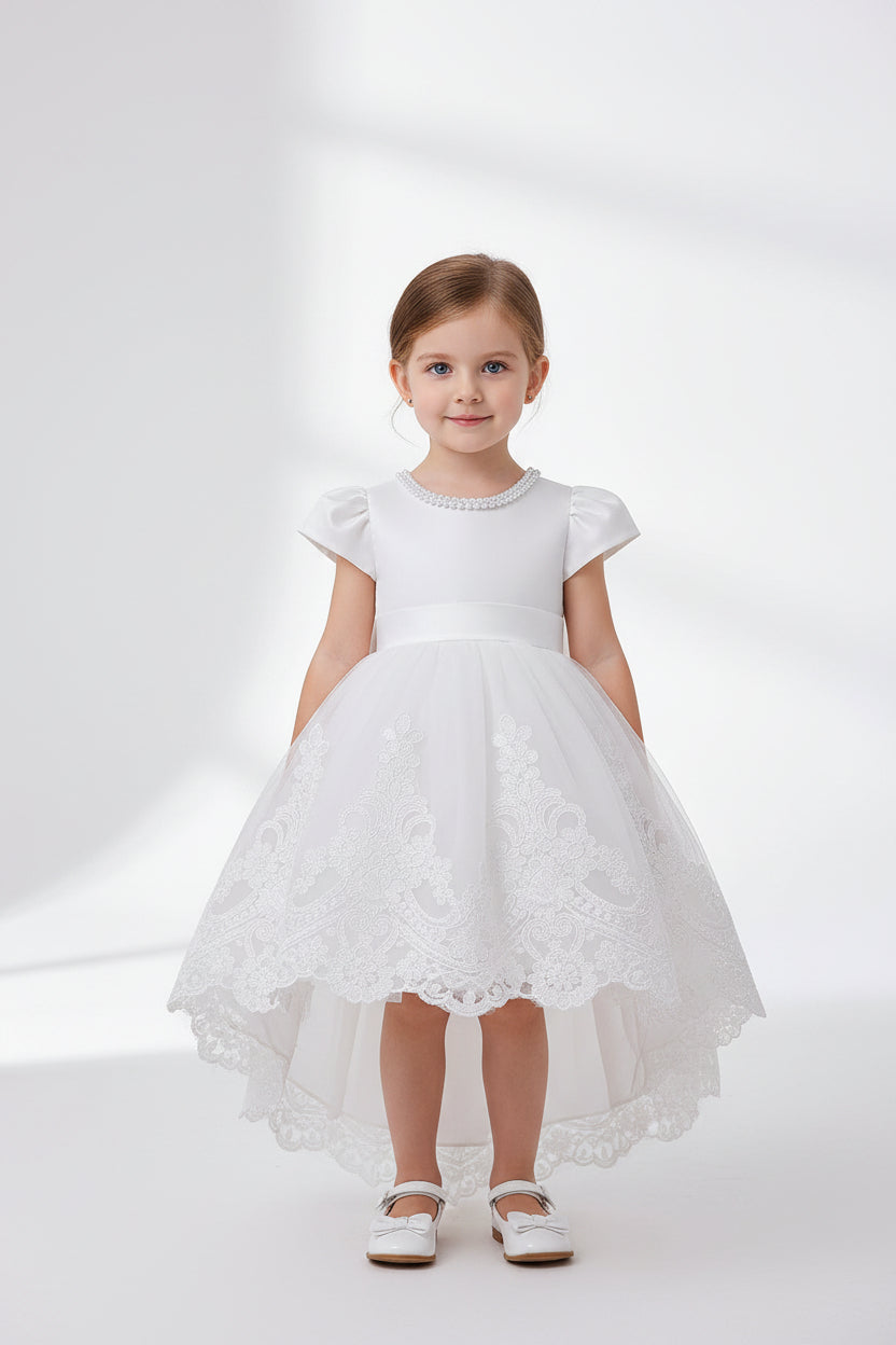 Toddler girl wearing a white lace high-low formal dress with puff sleeves and pearl neckline, available at Trendy Angels Boutique.